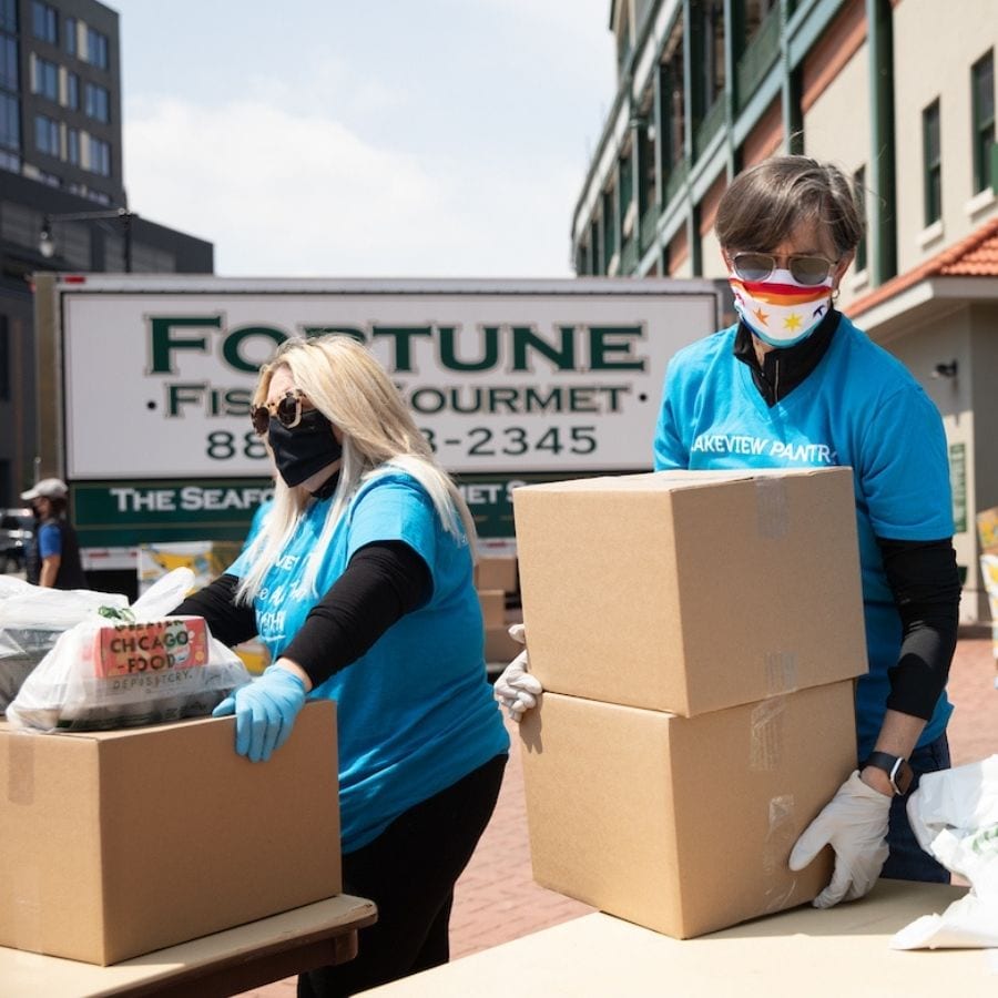 Two volunteers wearing masks lift cardboard boxes of food at Lakeview Pantry