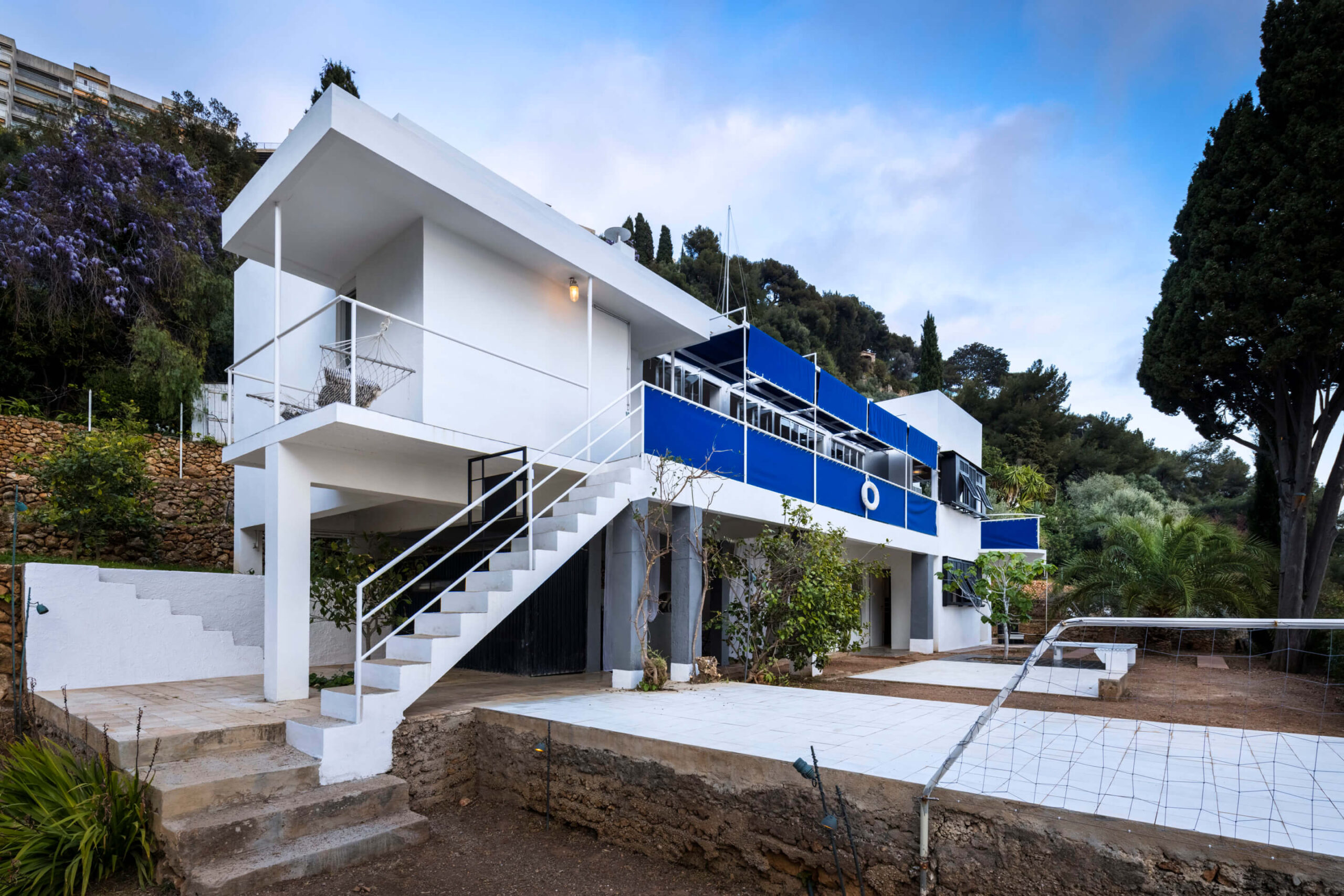 The facade of Eileen Gray's Villa E-1027. The cubist villa is bright white with touches of vibrant blue canvas covering open walkways.