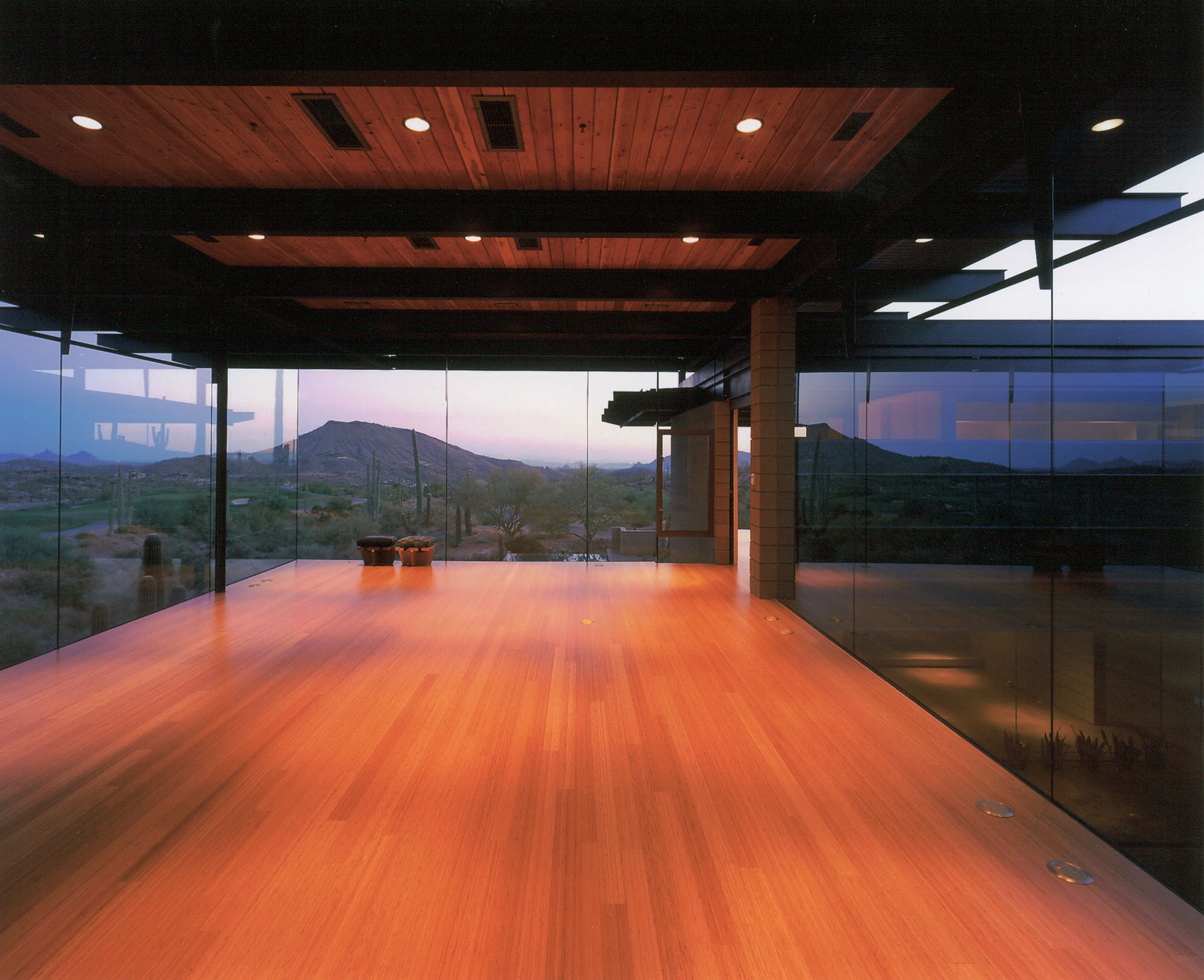 A tranquil corner of the home looks out through glass curtainwalls to the sprawling desert landscape at dusk.
