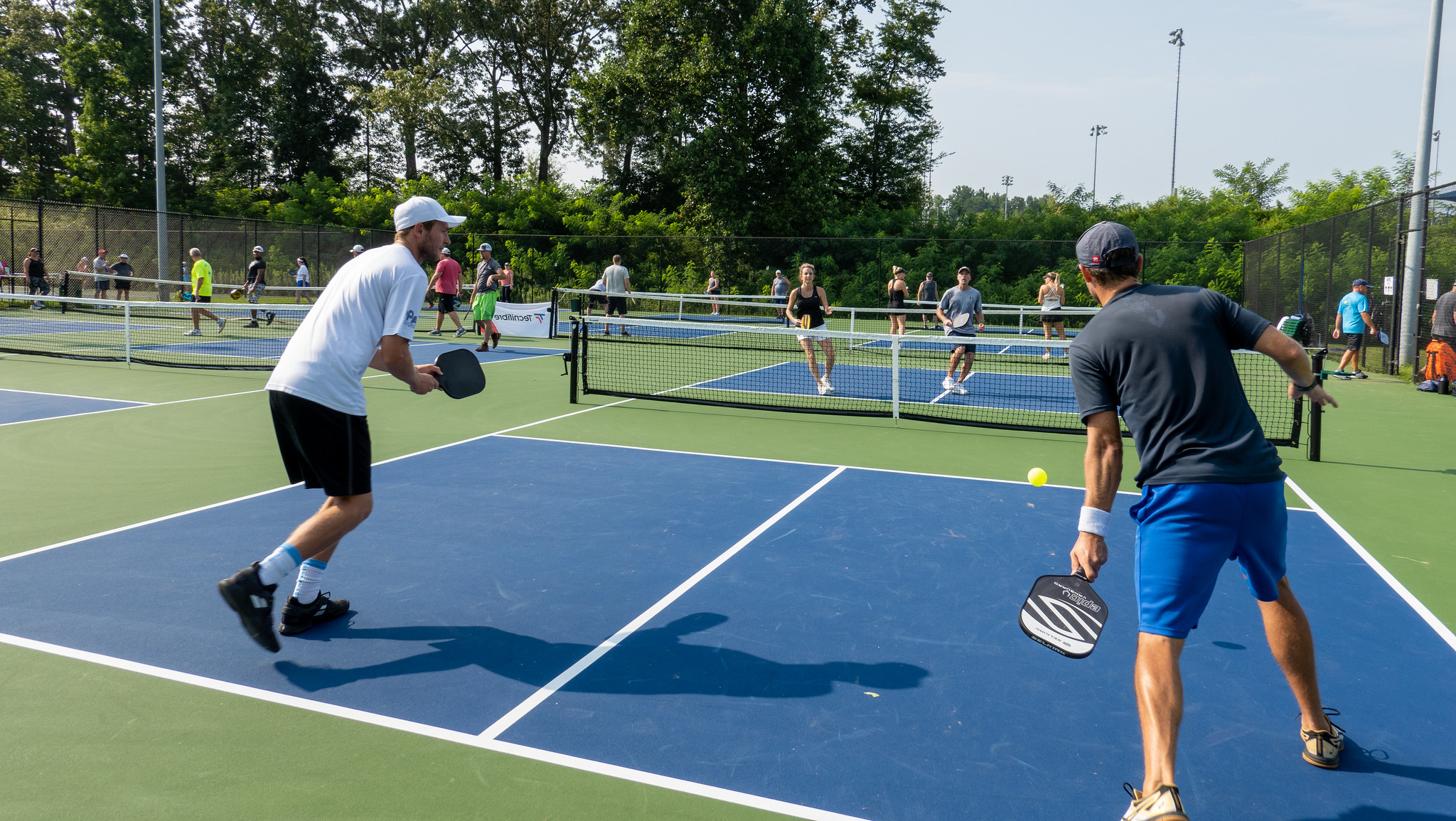 A group of people play pickleball in a sun filled court
