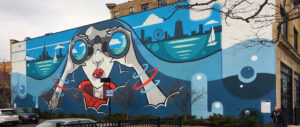A mural painted on a the side of a brick building depicts a woman gazing onto Lake Michigan with the skyline of Chicago behind her.
